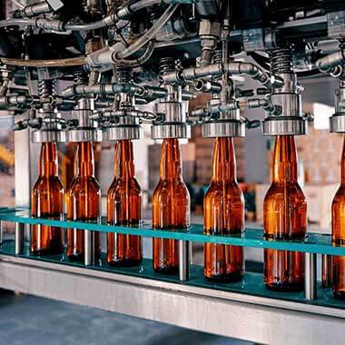 Bottiglie di vetro movimentate attraverso un impianto di produzione di bevande. Il monitoraggio della durezza dell'acqua è importante per la gestione della qualità del prodotto.